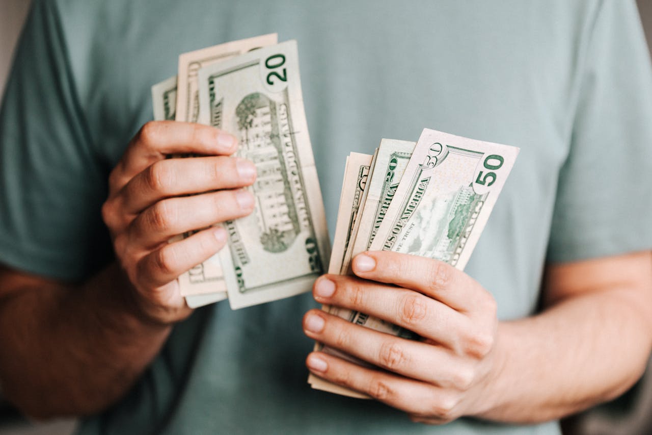 Crop anonymous male in casual tshirt holding dollar banknotes counting money with hands